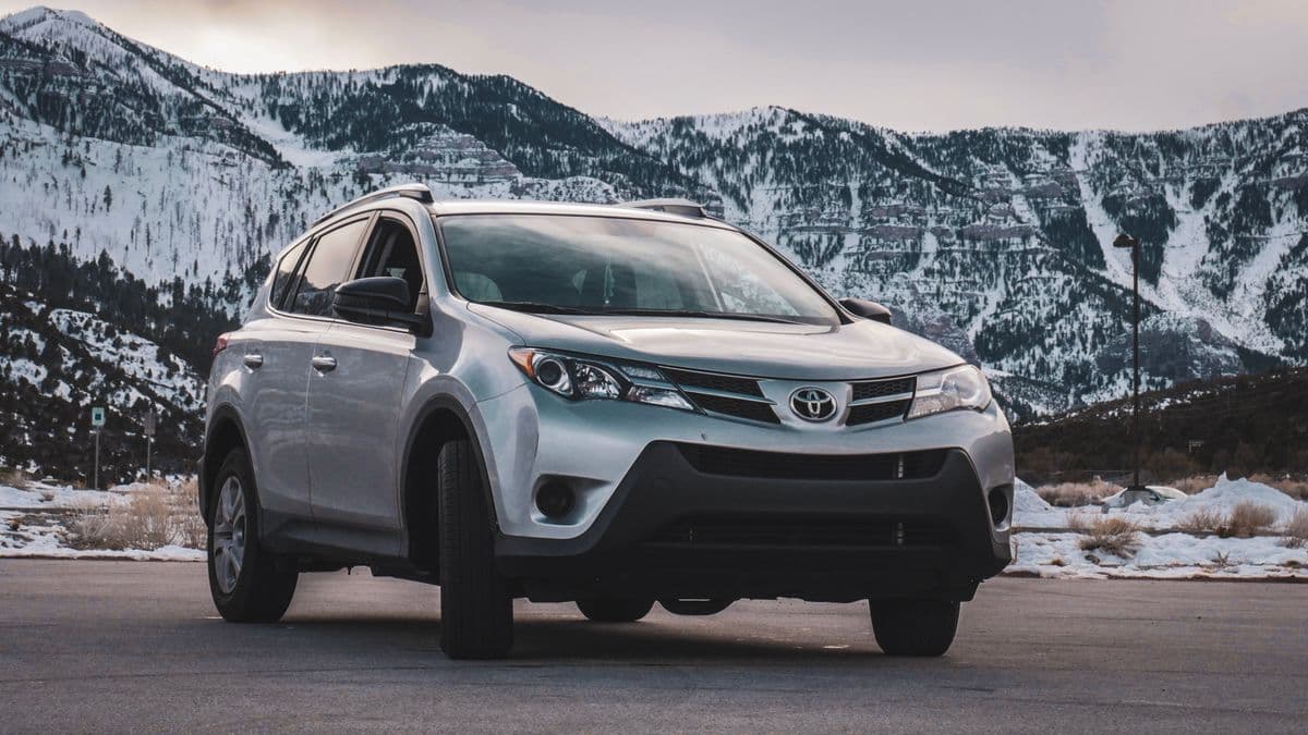 A silver crossover parked in front of a snow covered mountain range